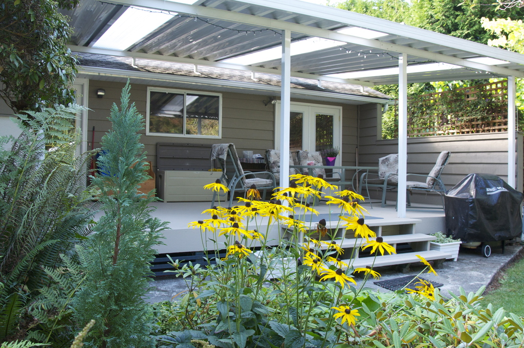 Roof-covered patio, with an outdoor table and chairs, facing the backyard