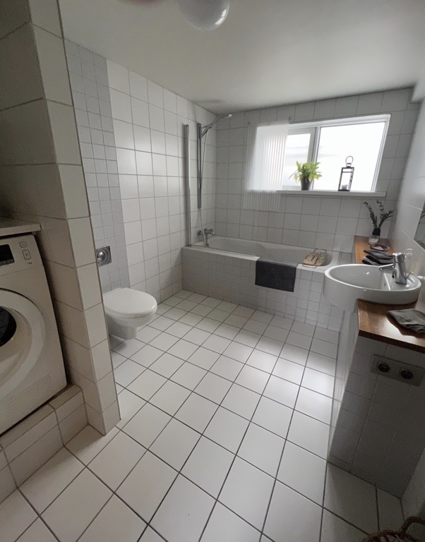 The bathroom is spacious with toilet, basin and bathtub with a shower. 