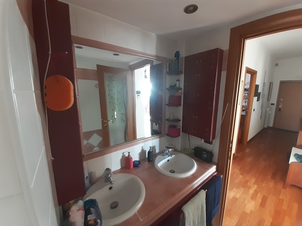 Part of the bathroom, with twin sinks, and a view of the corridor and main door