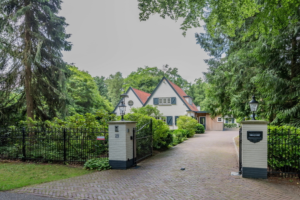 De voorkant van het huis, het terrein is met een ijzeren hek begrensd. 