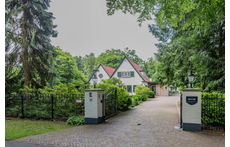 De voorkant van het huis, het terrein is met een ijzeren hek begrensd. 