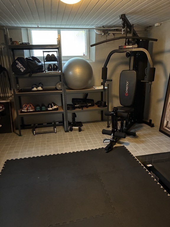 Exercise room in the basement with spinning bike, treadmill, yoga mat and weights.