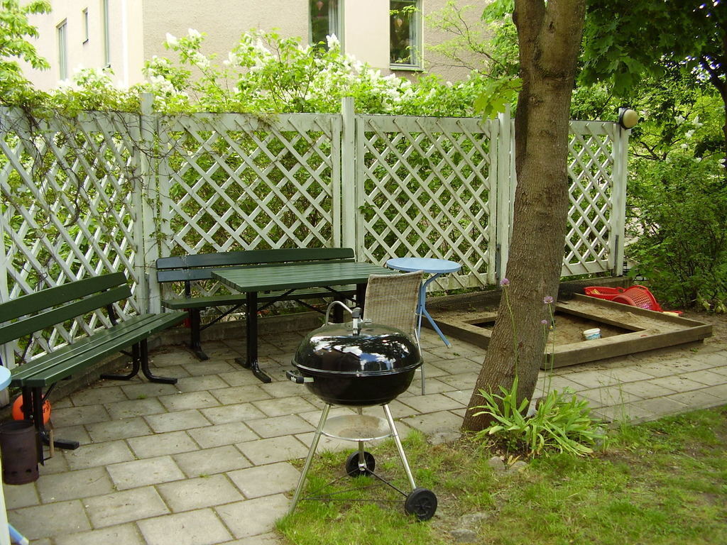 Andra sidan av trädgården med liten sandlåda, leksaker och en grill.