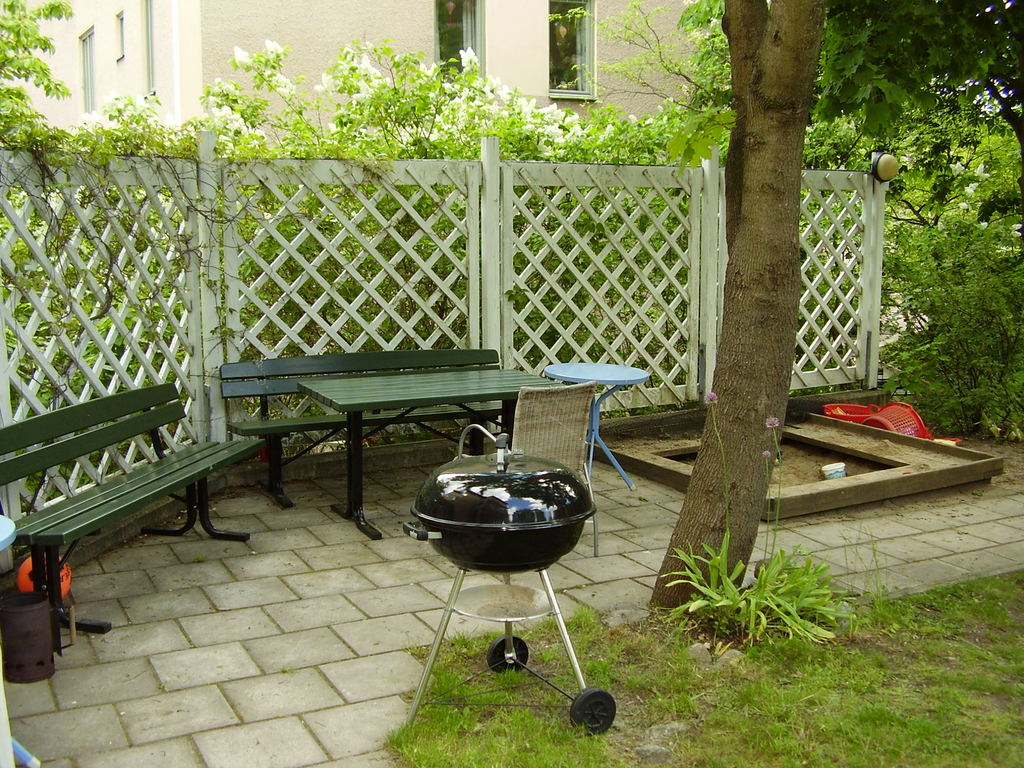 Andra sidan av trädgården med liten sandlåda, leksaker och en grill.