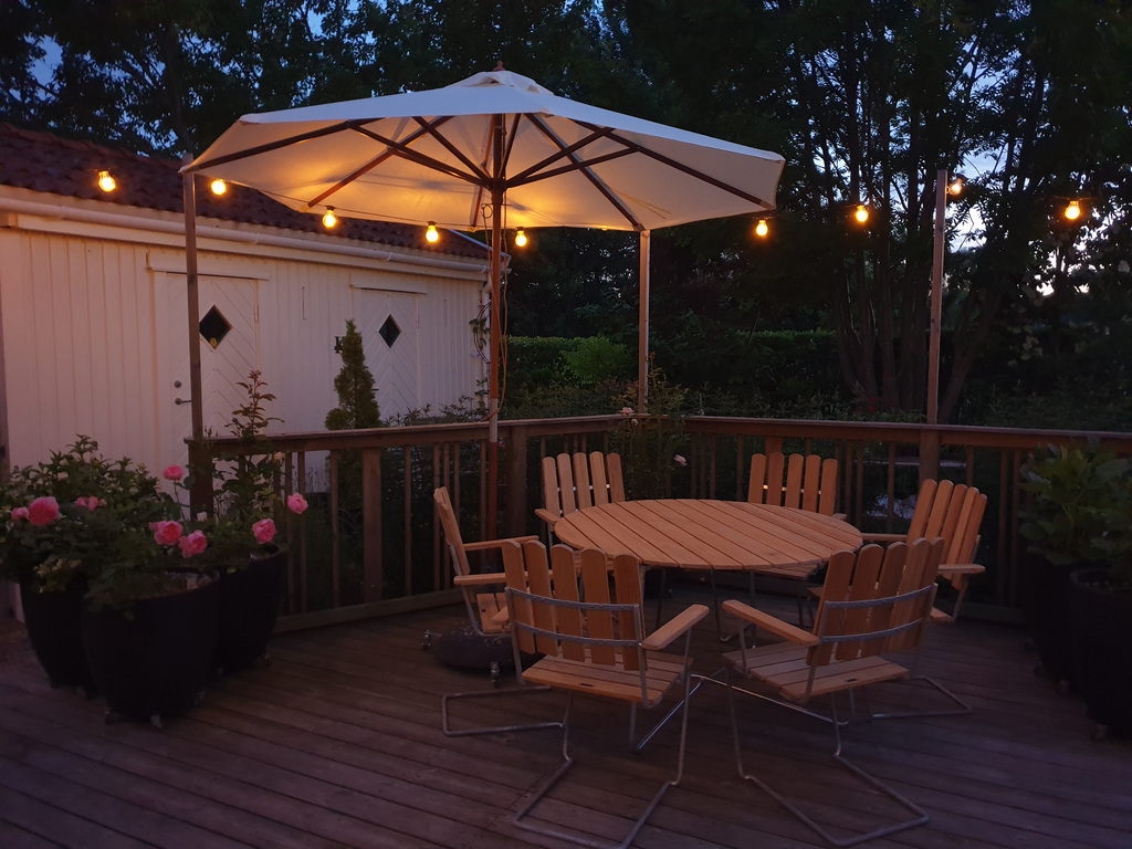 The large patio outside the kitchen, by night. Seating area, bbq and hanging chairs.