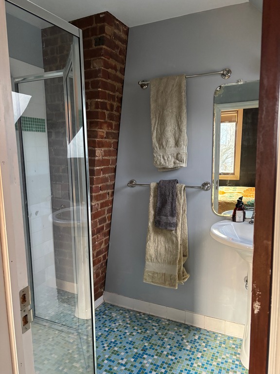 Third floor full bathroom has glass tile floor, exposed brick and skylight. 