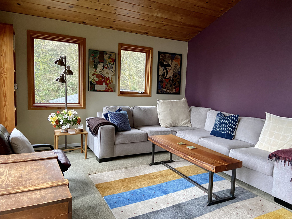 An upstairs large living room with a wall of windows looking out at Puget Sound. We see quite a few container ships go headed...