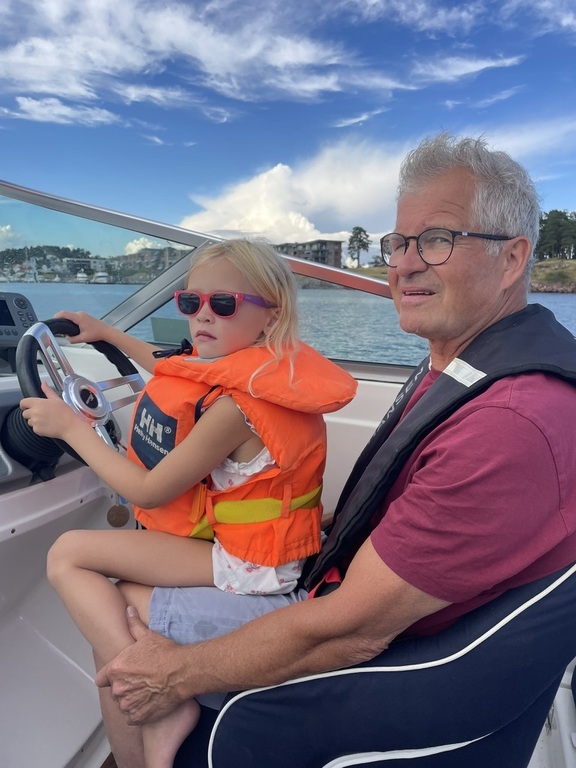 Linnea sitter på farfars fang og kjører båten i skjærgården utenfor Tønsberg